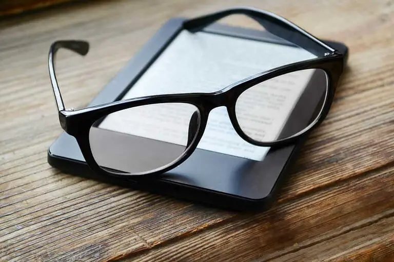 Black e-reader with glasses on a wooden table